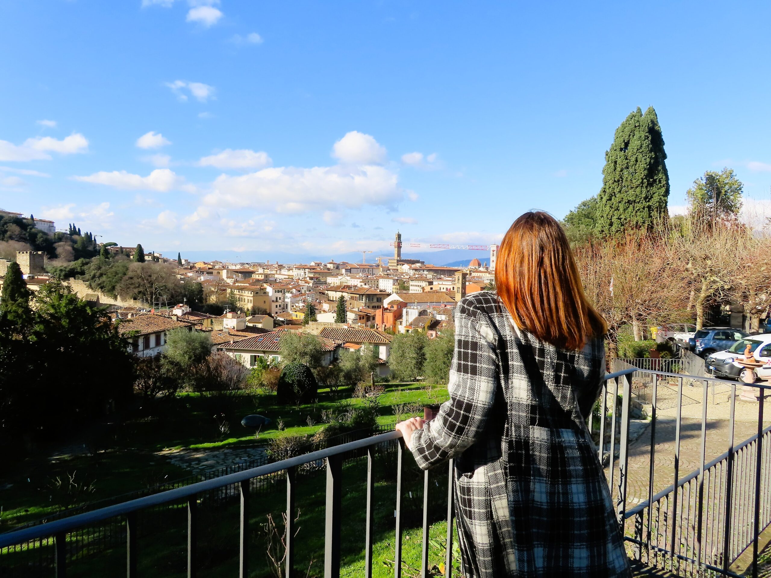 Francesca overlooking the rooftops of Florence from a scenic viewpoint, wearing a black and white plaid coat on a sunny winter day.